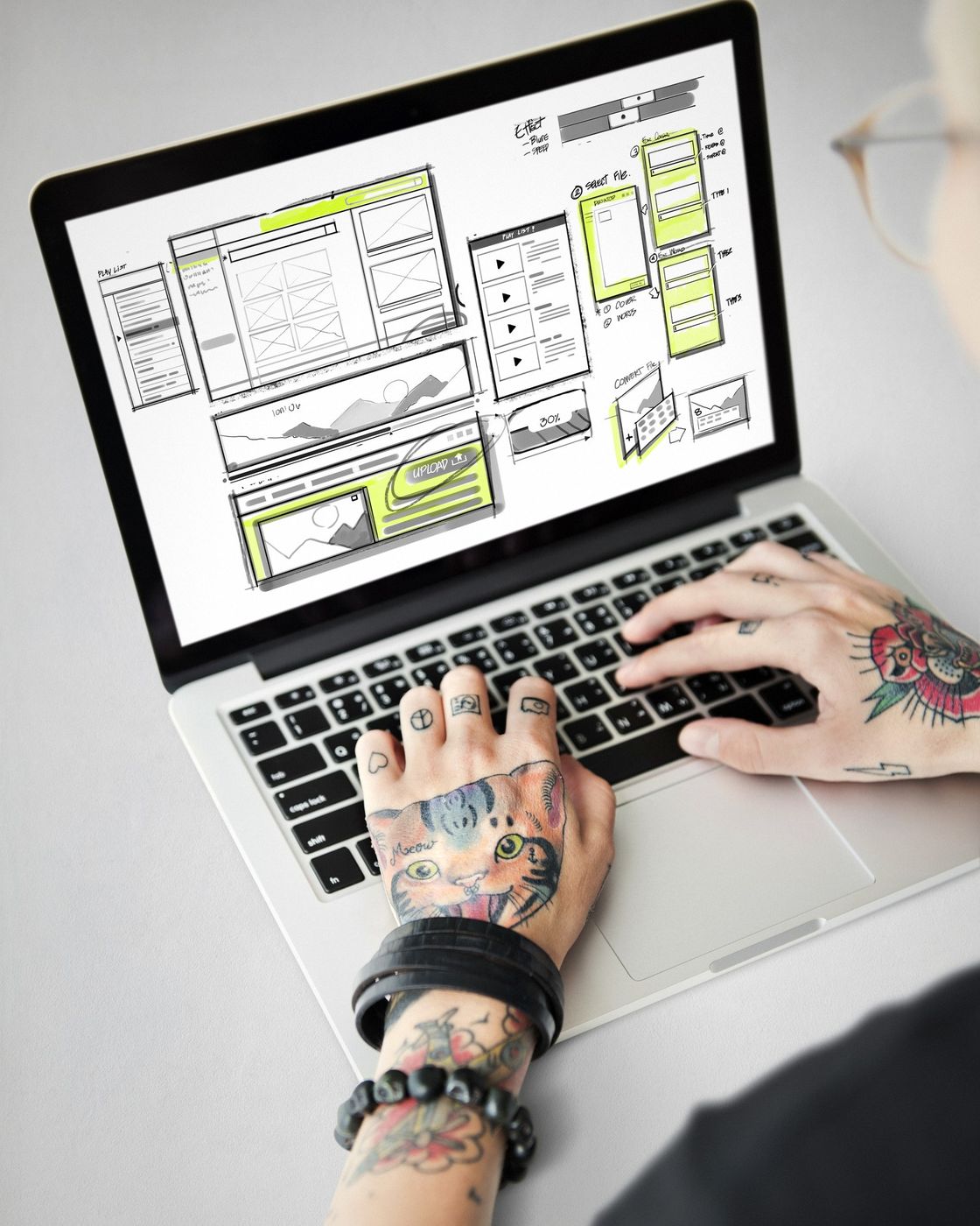 A designer's hands typing on a laptop displaying a website wireframe layout