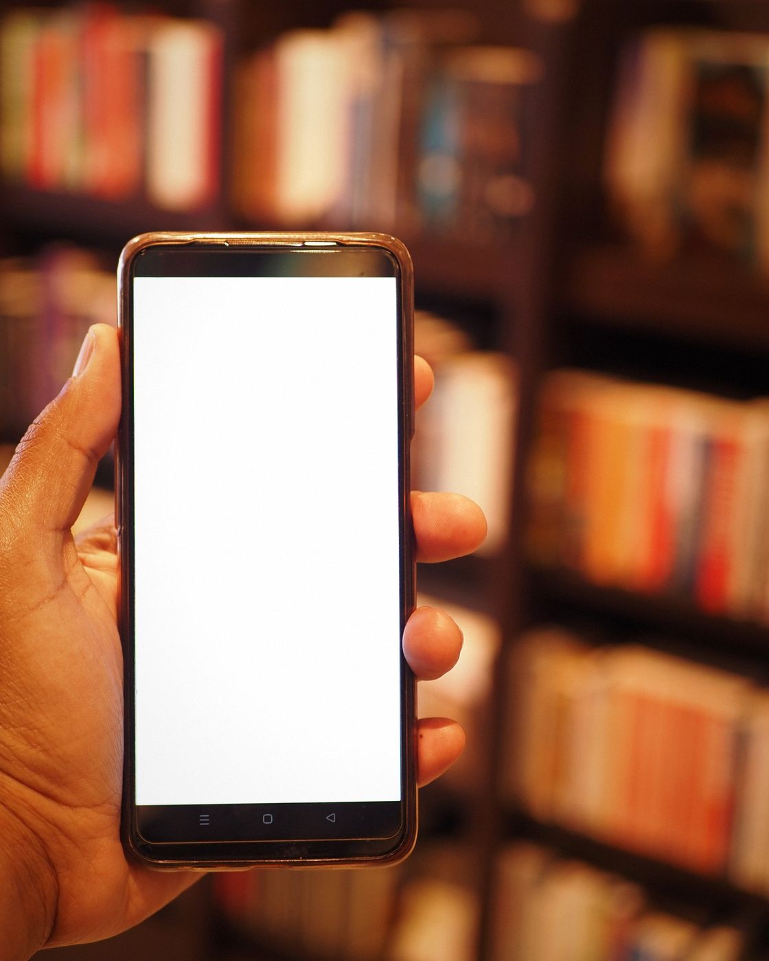 A hand holding a smartphone in front of a bookshelf, promoting a book online