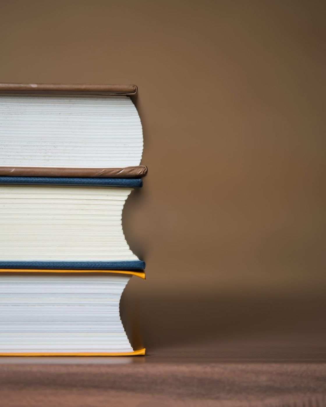 A neat stack of three hardcover books resting on a warm wooden table