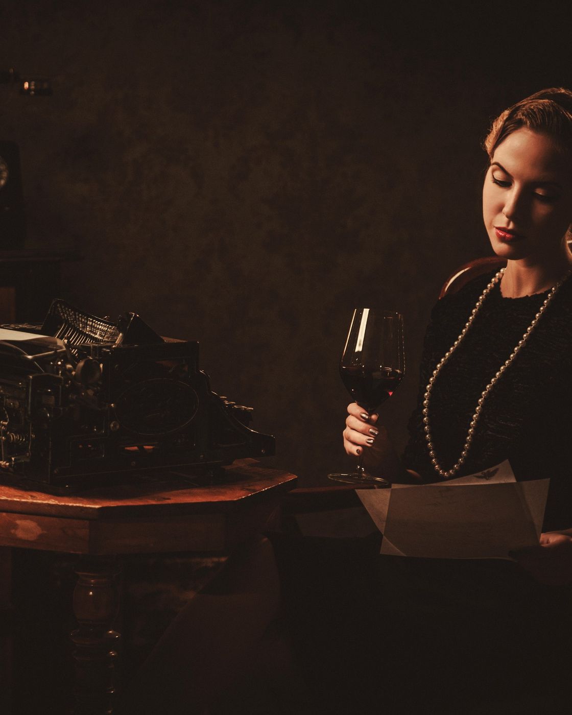 A noir-lit author reviewing a manuscript beside a vintage typewriter, glass of wine in hand