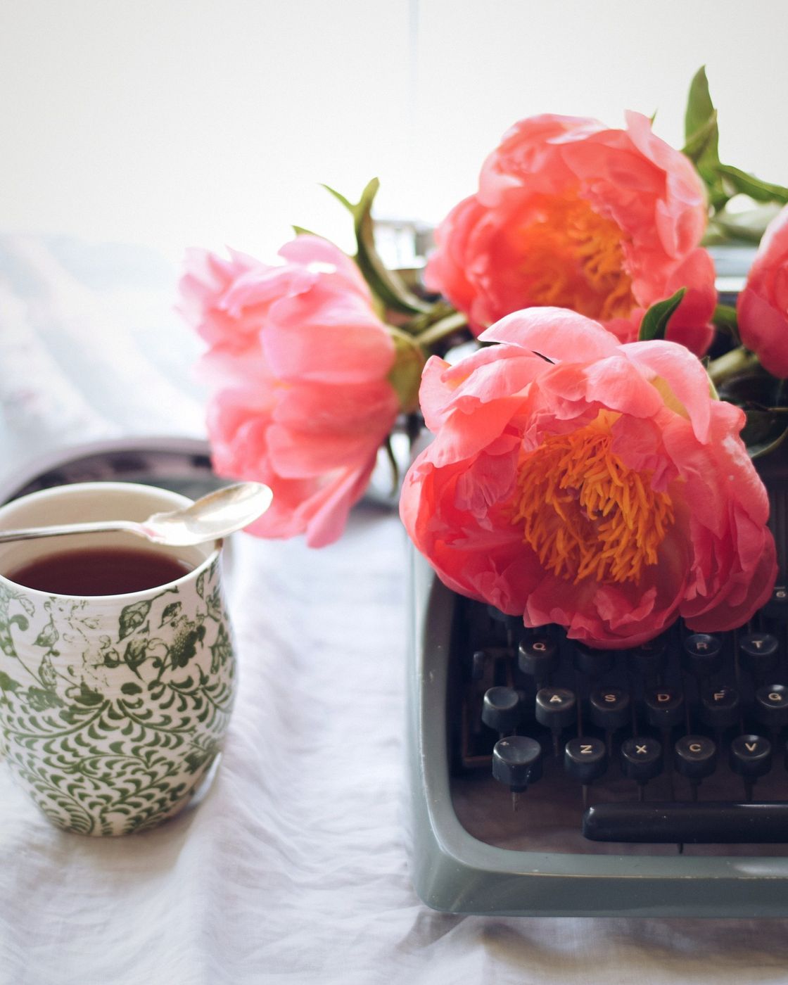 Pink peonies and a cup of tea resting on an antique typewriter