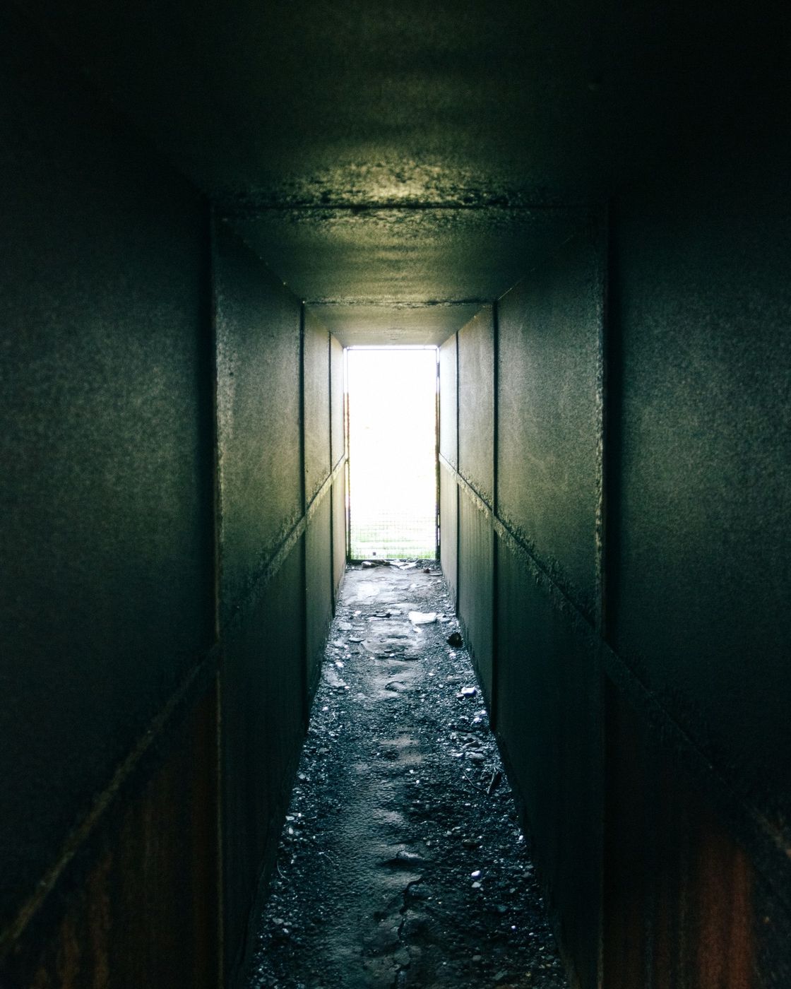 A dark, narrow tunnel leading toward a distant glow of light