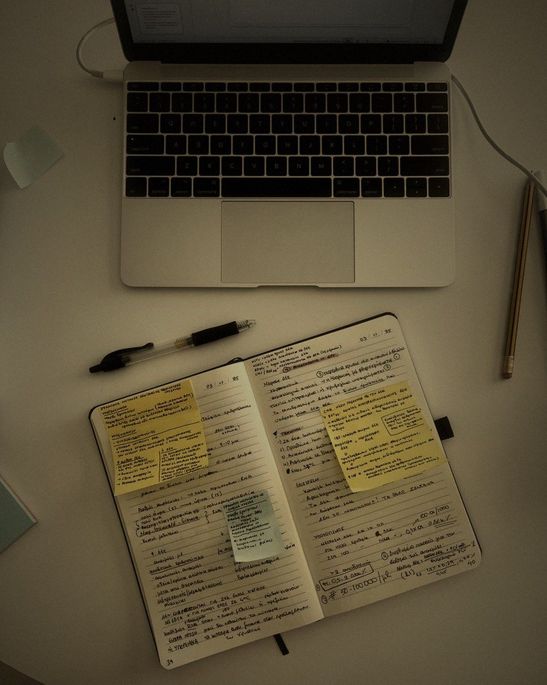 An open planner covered in sticky notes next to a laptop, warm desk lamp light