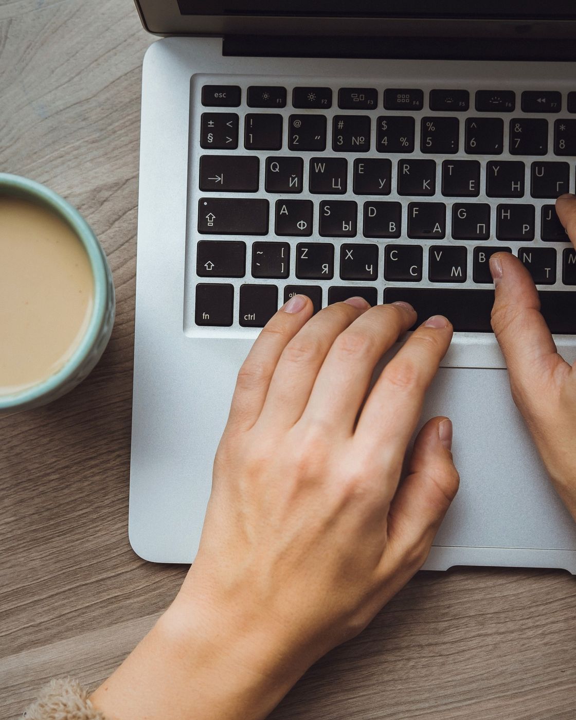 Hands typing on a laptop keyboard beside a cup of coffee