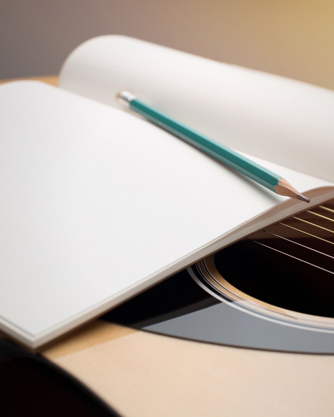 An acoustic guitar with an open notebook and pencil across its strings