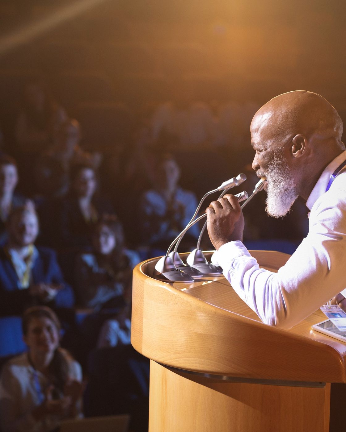 An author speaking at a podium in front of a lit audience